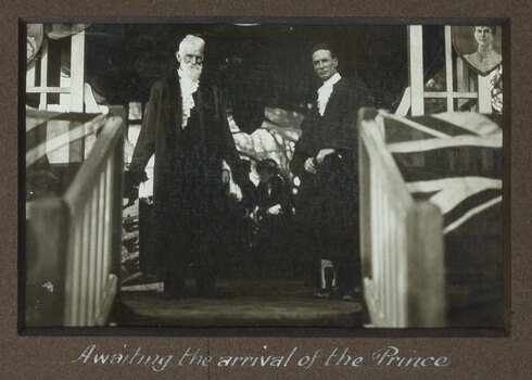 Black and white photograph of 2 men in ceremonial robes standing at the top of a stair case.