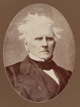 Sepia photograph of the Honorable George Ward Cole as an elderly man with ruffled white hair in a dark suit, looking towards photographer. 