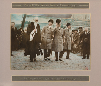 Coloured photograph of a row of four men, one in ceremonial robes and three in bowler hats. Man in centre is raising his hat to the surrounding crowd.