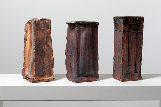 Three bronze and orange coloured rectangle shaped vases on a white ledge