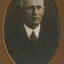 Black and white photograph of a man with grey hair in a dark suit and patterned tie