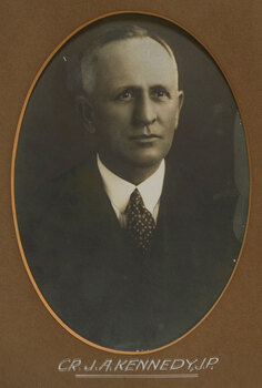 Black and white photograph of a man with grey hair in a dark suit and patterned tie