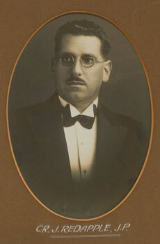 Black and white photograph of a man with dark hair and glasses wearing a dark suit and bow tie