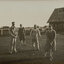 Black and white photograph of four men playing golf, a small building in the background
