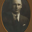Black and white photograph of a man with short dark hair in a dark suit and tie
