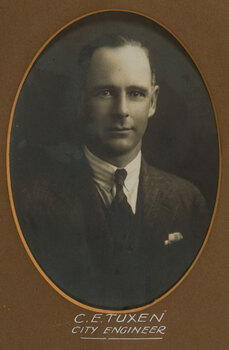 Black and white photograph of a man with short dark hair in a dark suit and tie