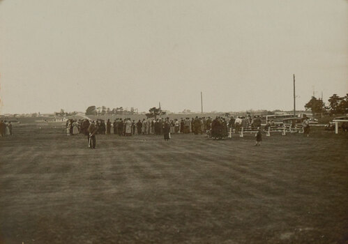 Black and white photograph of people playing golf, a large crown in the background facing away from the photograph