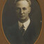 Black and white photograph of a man with grey hair in a dark suit and tie