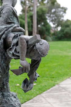Close up of a metal sculpture of a child holding paper boats in his hands.