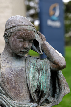 Close up of a metal sculpture of a child holding a shell to his ear