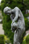 Bonze sculpture of a classical female figure who holds a vessel and looks downward. There are trees in the background.