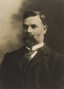 Black and white photograph of a bearded man in a suit and tie.