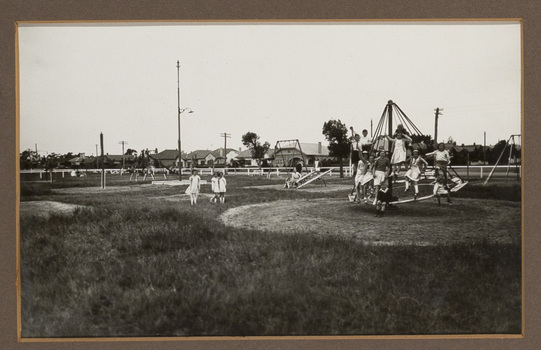 Black and white photograph of children posing at a playground with houses in the background