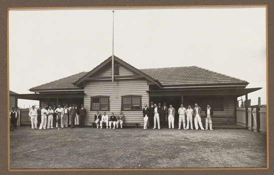 Black and white photograph of men in cricket uniform in front of a sporting club house