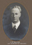 Black and white photograph of an oval portrait of a man in with white hair