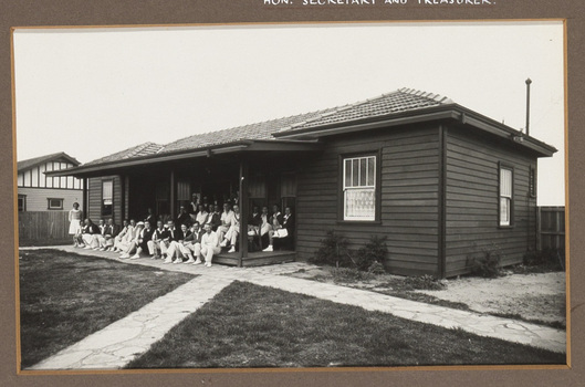 Black and white photograph of women and men in tennis outfits, posing in front of a sporting club house