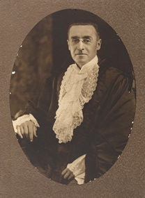 Sepia oval photograph of a formal portrait of a seated man with glasses wearing mayoral robes with fur trims and lace cuffs and jabot.