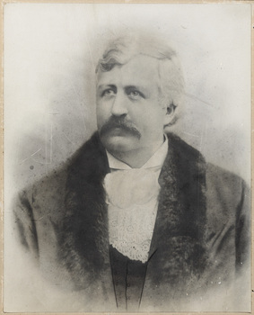 Black and white formal portrait photograph from chest up of man with white hair and a moustache wearing mayoral robe with fur trim and lace jabot.