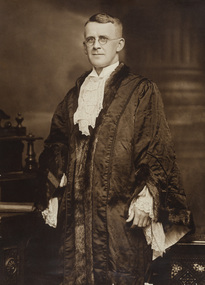 Black and white photograph of a formal portrait of a standing man wearing a mayoral robe with fur trim and lace cuffs and lace jabot. 