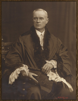 Black and white photograph of a formal portrait of seated man wearing mayoral robes with fur trims and lace cuffs with white shirt. 