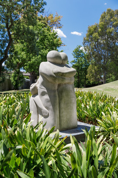 Photograph of an outdoor stone sculpture of three stylized figures embracing within a park setting.