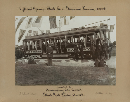 Black and white photograph of a tram with passengers aboard and crowds of people to the left. Mounted on grey card with handwritten text above and below.