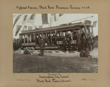 Black and white photograph of a tram with passengers aboard and crowds of people to the left. Mounted on grey card with handwritten text above and below.
