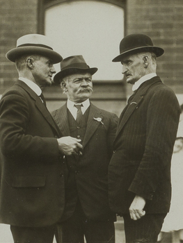 Black and white photograph of three men in suits in conversation