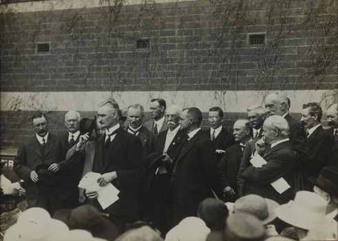 Black and white photograph of a group of suited men addressing a crowd