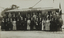 Black and white photograph of a group of suited men and women posing by a tram