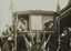 Black and white photograph of a woman leaning out of the front window of a tram cutting a ribbon