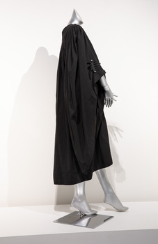 Photograph taken from the side of a plain black ceremonial robe on a silver mannequin