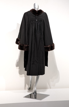 Photograph taken from the back of a black ceremonial robe with fur trim on a silver mannequin.