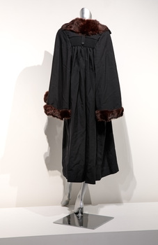 Photograph taken from the back of a black ceremonial robe with brown fur trim on a silver mannequin.