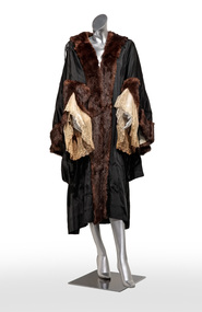 Photograph of a black ceremonial robe with brown fur edging and cream and lace cuffs on a silver mannequin.