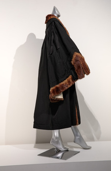 Photograph taken from a side view of a black ceremonial mayoral robe with brown fur trim on a silver mannequin.