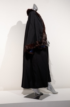 Photograph taken from the side of full length black ceremonial mayoral robe with dark fur trim on a silver mannequin.