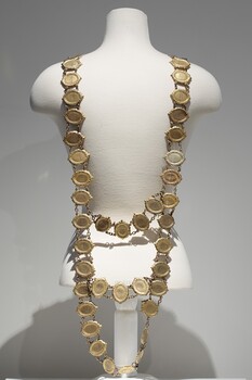 Photograph taken of the back of a gold ceremonial Mayoral chain on a cream torso. The chain consist of small oval links with 2 rows connecting the links at the back