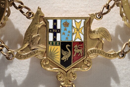 Photograph of a gold and enamel coat of arms with chains linking it on either side