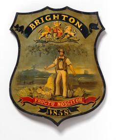 Photograph of a shield with a painted coat of arms for Brighton. A farmer stands surrounded by fruit, a train, ship and windmill are in the distance.