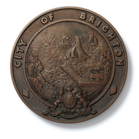 Round cast bronze plaque for City of Brighton crest, with a coastal scene in the centre and British Coat of Arms at the bottom.
