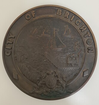 Round cast bronze plaque for City of Brighton crest, with a coastal scene in the centre and British Coat of Arms at the bottom.