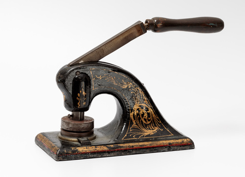 Black metal seal press with wooden handle, decorated with gold painted scrolls,