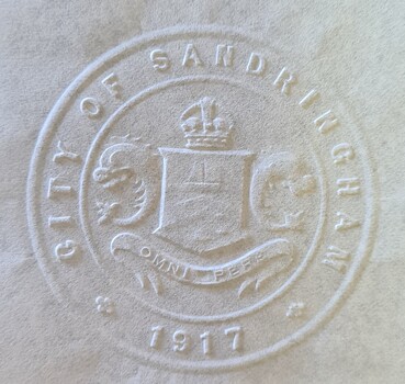 Embossed round seal for "CITY OF SANDRINGHAM" onto white paper containing coat of arms in centre