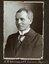 Black and white photograph of a man in a suit with his name written underneath on the mount