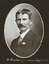 Black and white oval photograph of a man in a suit with his name written underneath on the mount