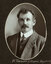 Black and white oval photograph of a man in a suit with his name written underneath on the mount