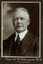Black and white photograph of a man in a suit with his name written underneath on the mount