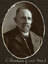 Black and white oval photograph of a man in a suit with his name written underneath on the mount