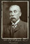 Black and white photograph of a man in a suit with his name written underneath on the mount